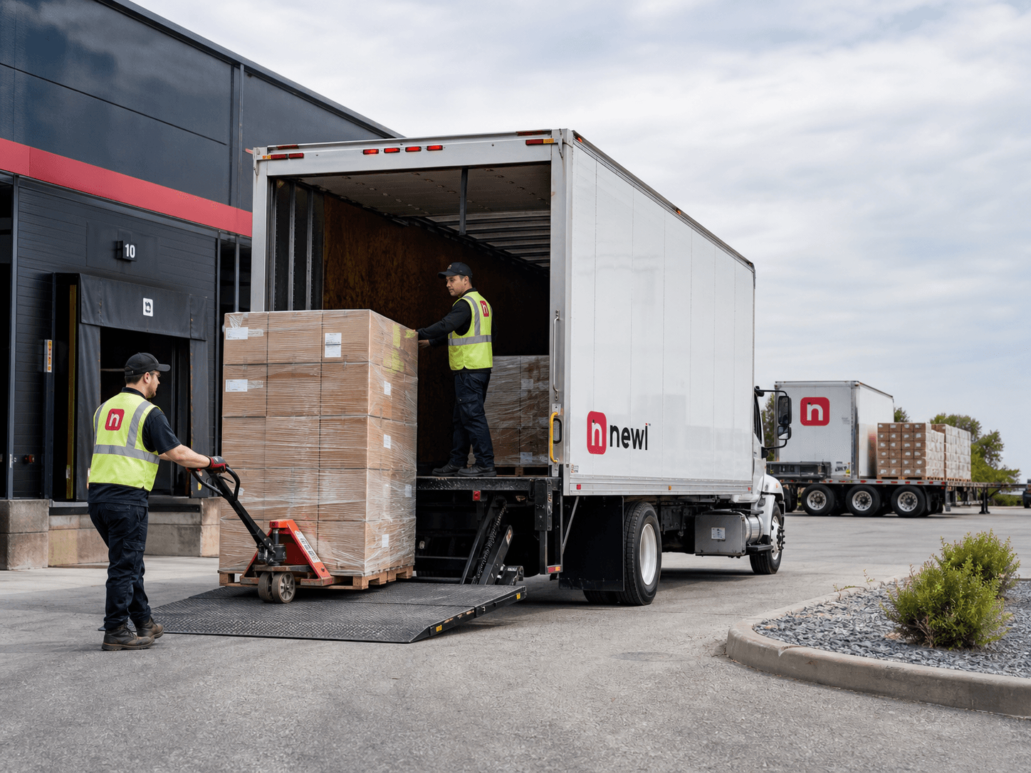 Newl local trucking team unloading palletized freight from a tailgate truck at a commercial receiving entrance